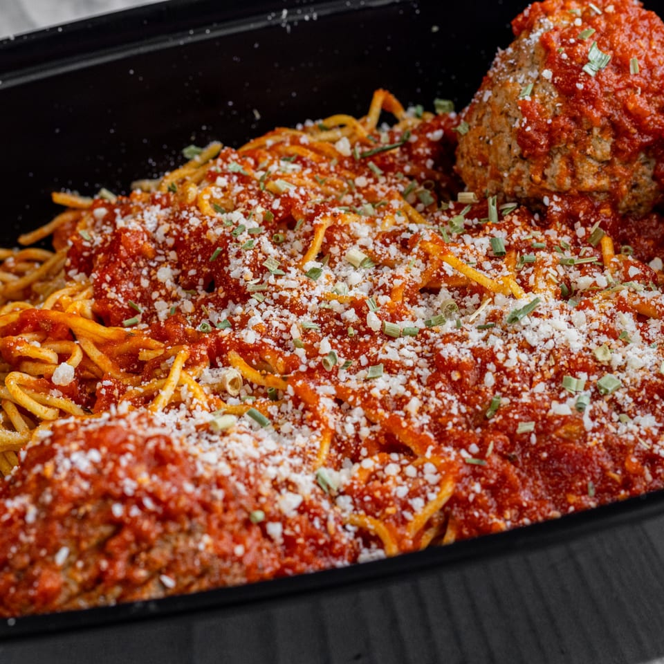 Spaghetti with meatballs, red sauce, parmesan cheese, and chives in a black container.