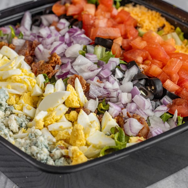 A vibrant Corbos Pasta and Pizza House salad with diced tomatoes, onions, olives, eggs, and cheese.