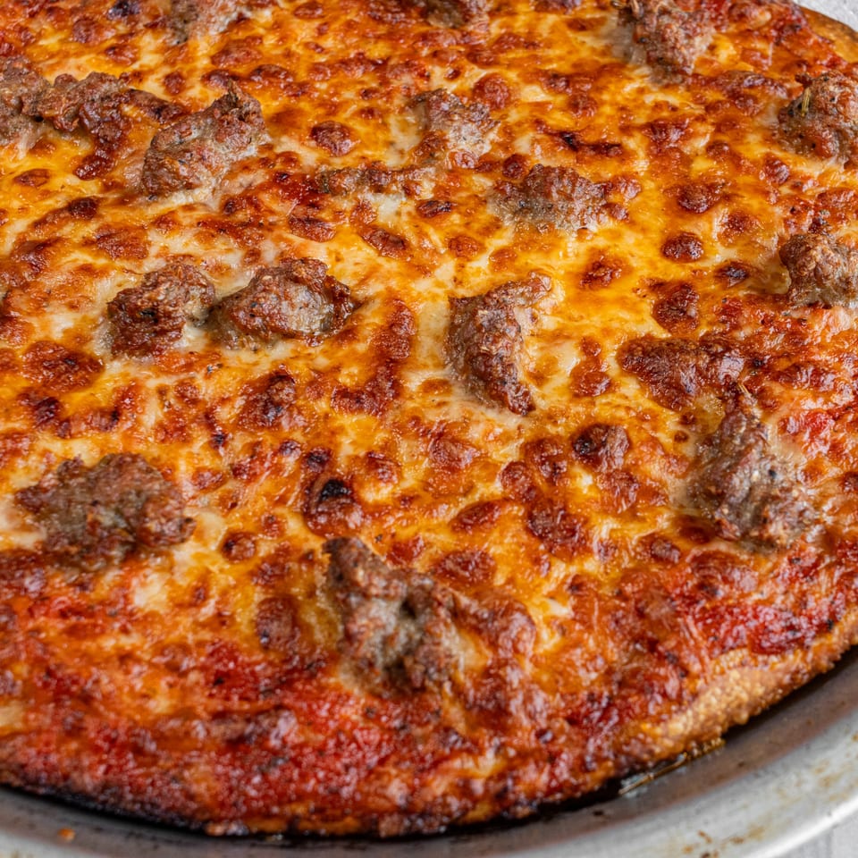 Close-up of a Corbos Pizza with melted cheese and generous crumbled sausage toppings.